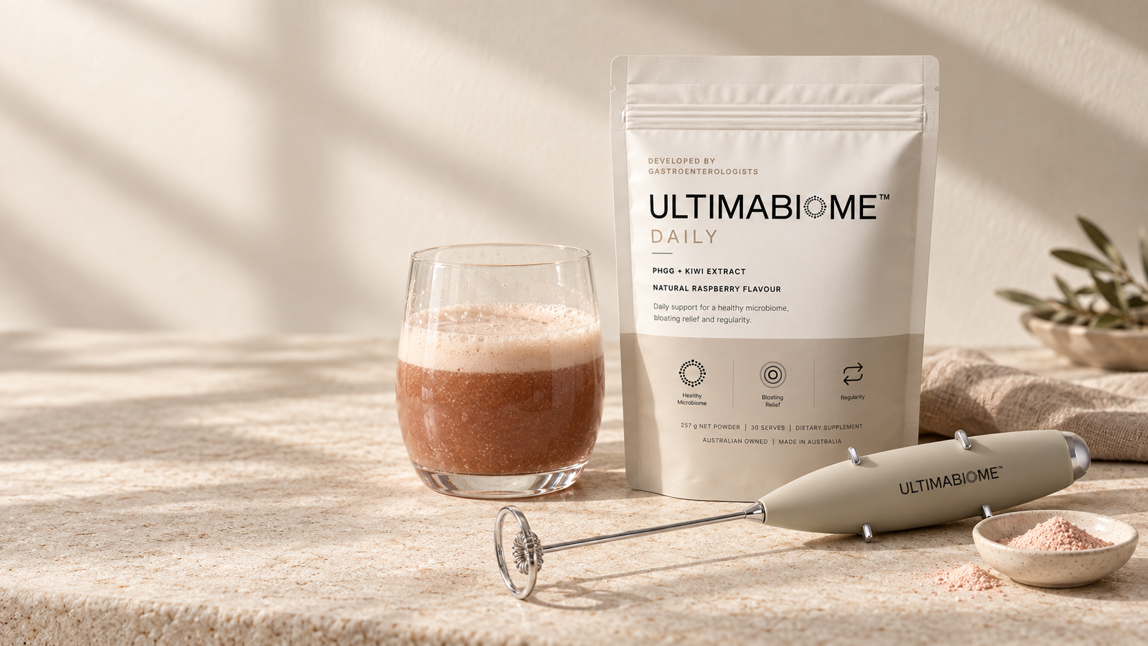 ULTIMABIOME Daily pouch with mixed raspberry serve, frother and powder on warm stone